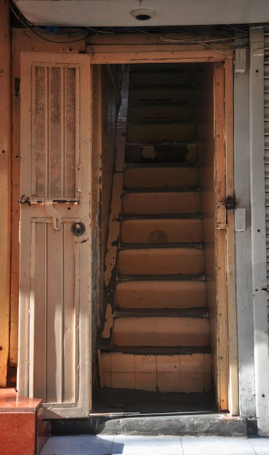 A narrow white porch or corridor with a series of evenly spaced white columns and a ceiling with hanging lantern-style lights. In the foreground, there is a black decorative wrought iron fence with a 